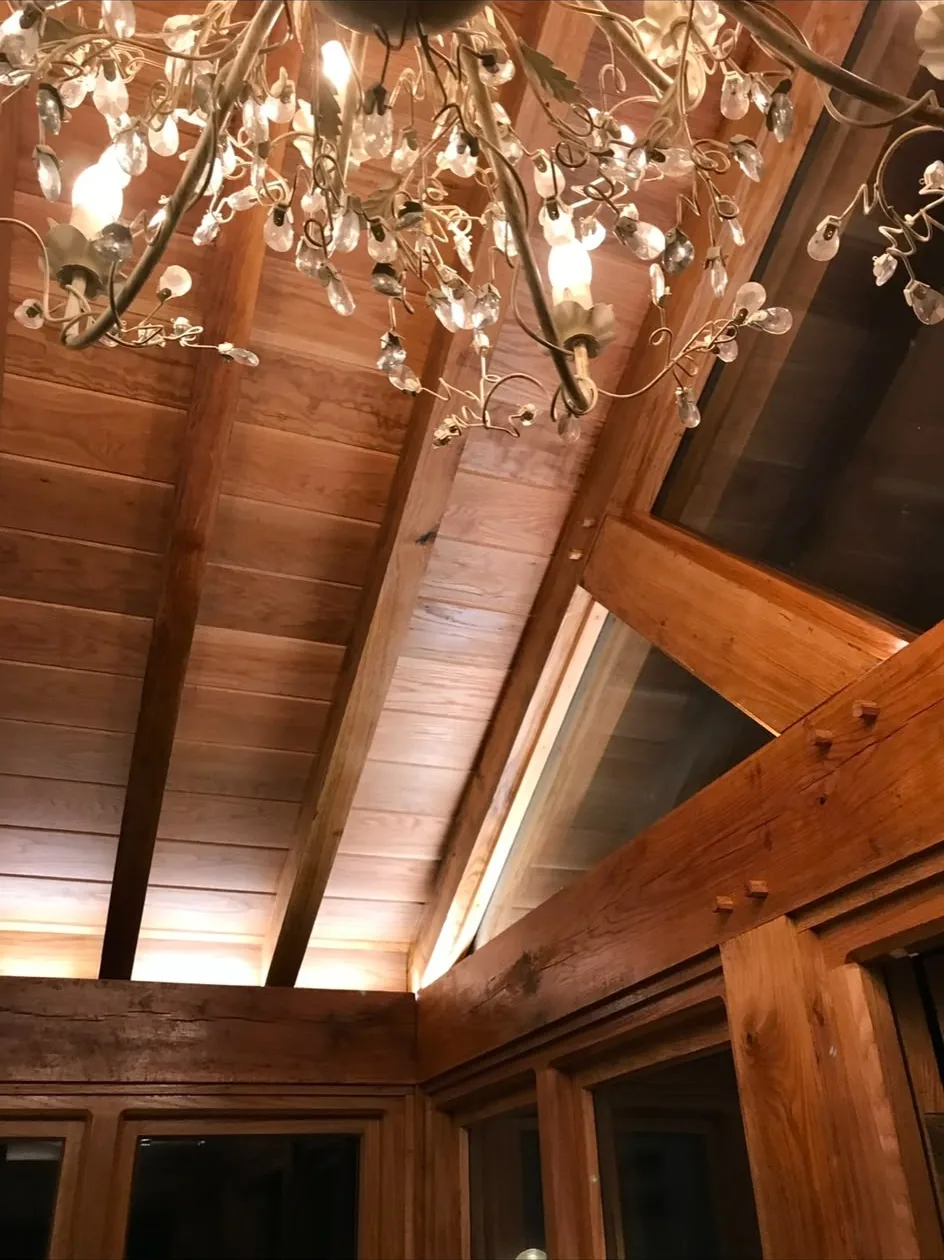 An oak-framed vaulted ceiling with exposed rafters, boarded soffit and pegged joints above a corner run of oak-framed windows.