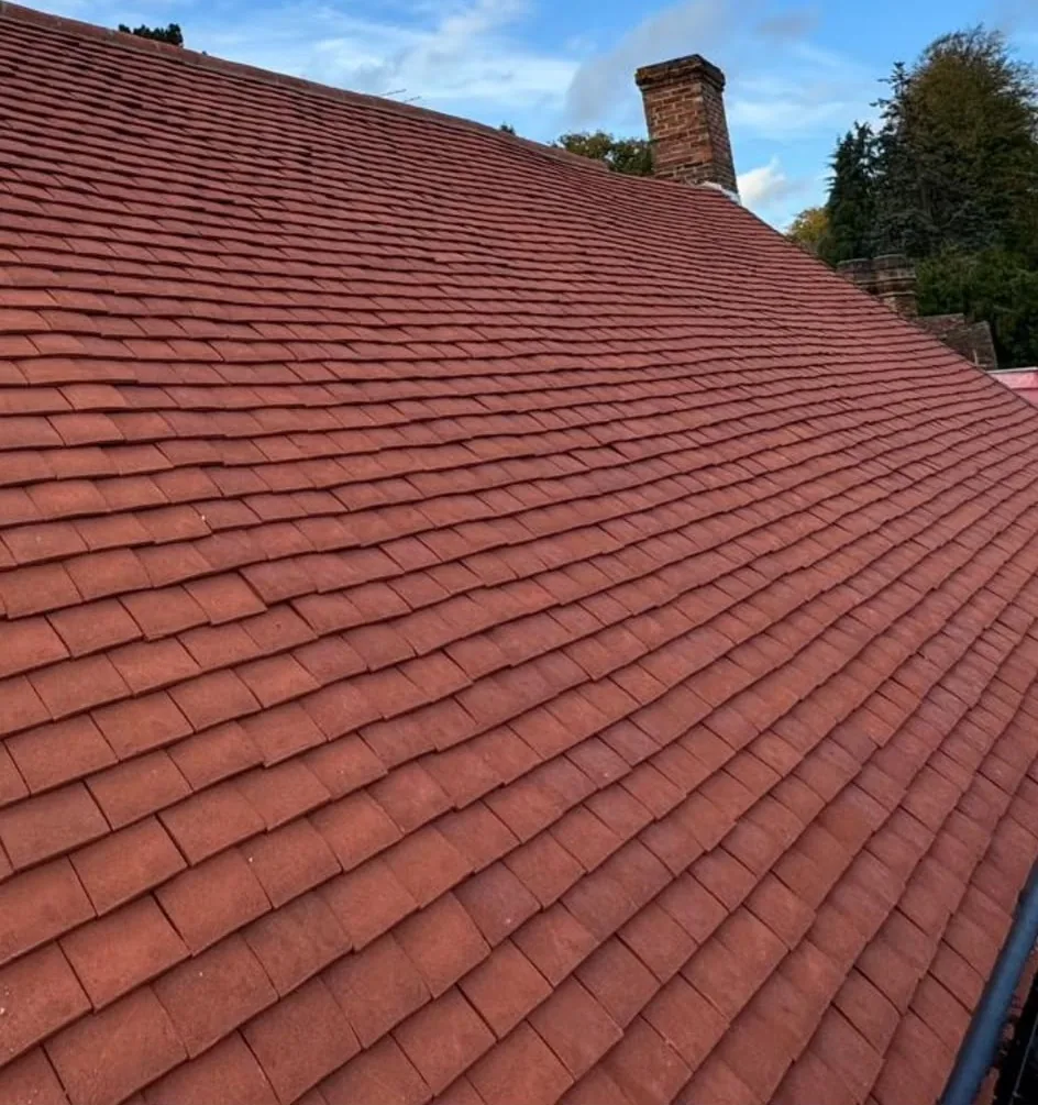A pitched roof newly covered in red clay plain tiles, running up to the ridge beside a brick chimney stack.