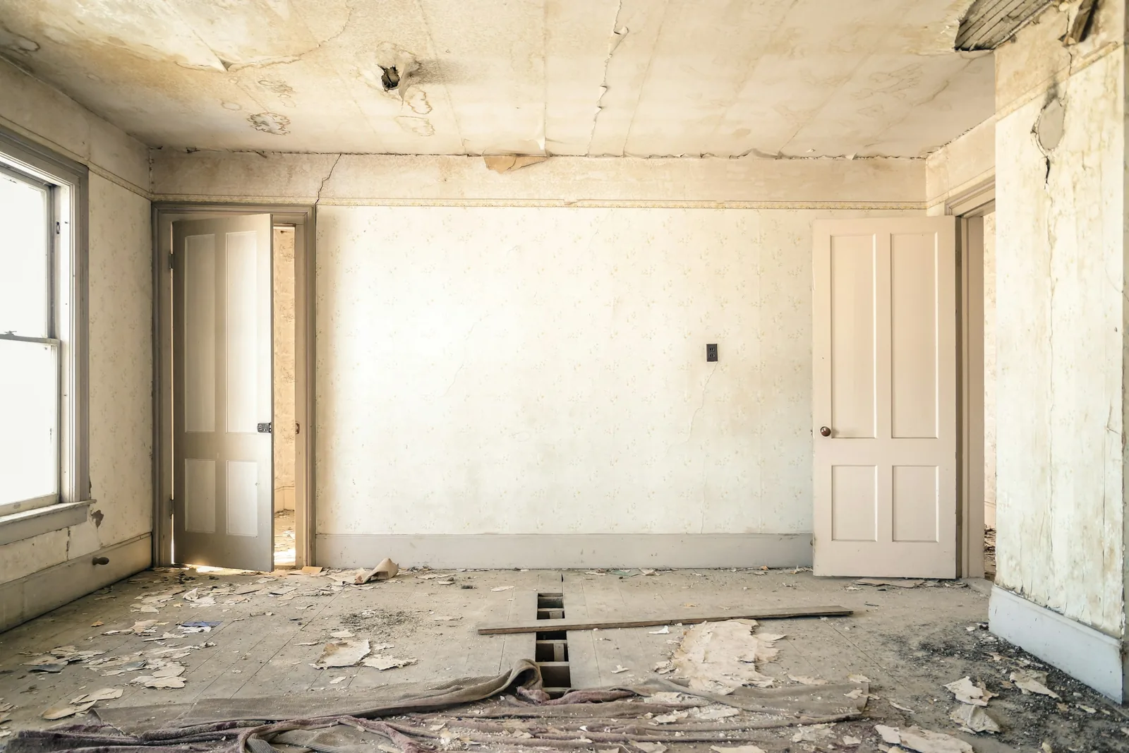 The ceiling paper has come away in water-stained strips above lifted boards and a rolled-back carpet.