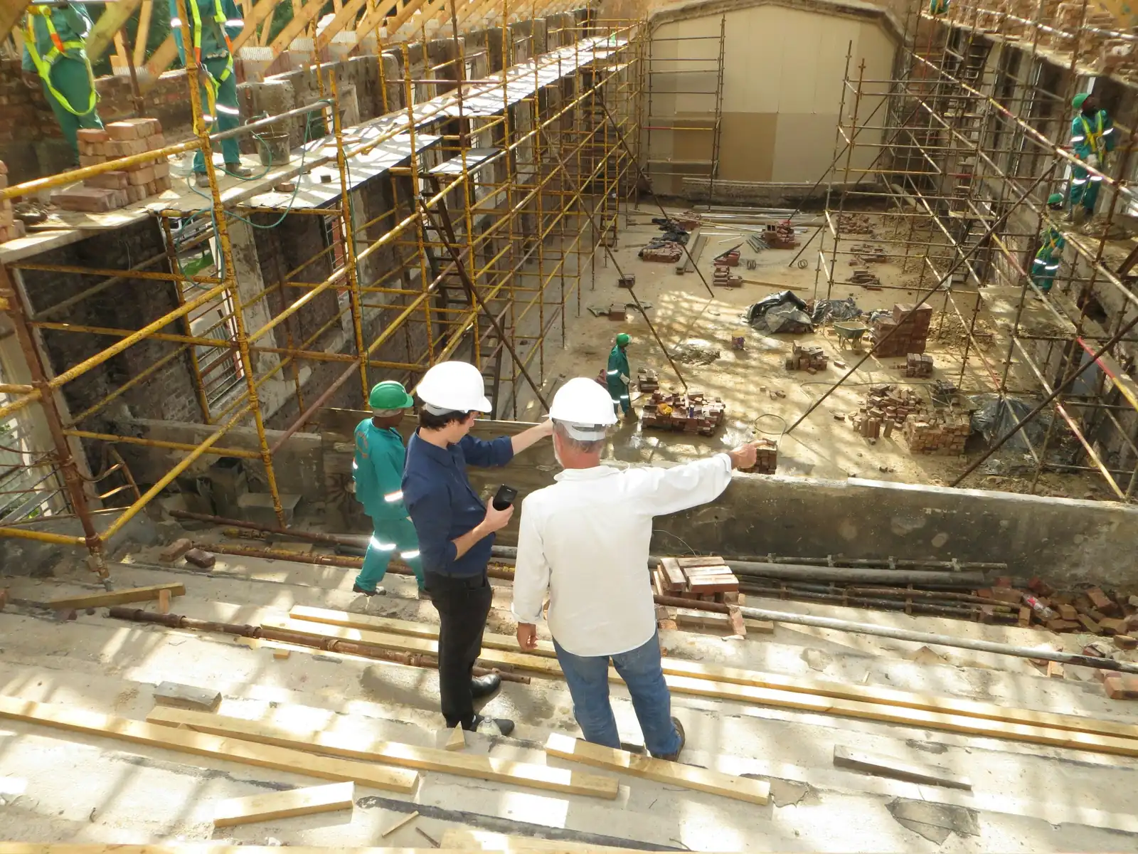 Two men in hard hats point down into a gutted shell where scaffold runs up both walls.