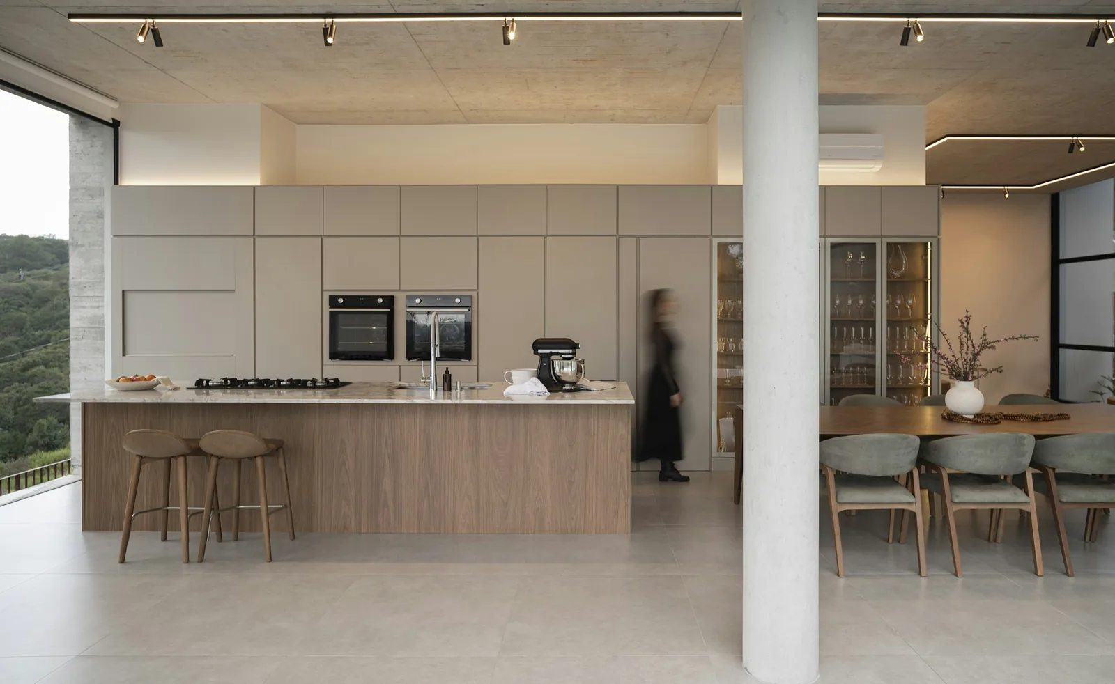 Stone worktop over a timber-clad island, with two ovens set into the tall run behind.