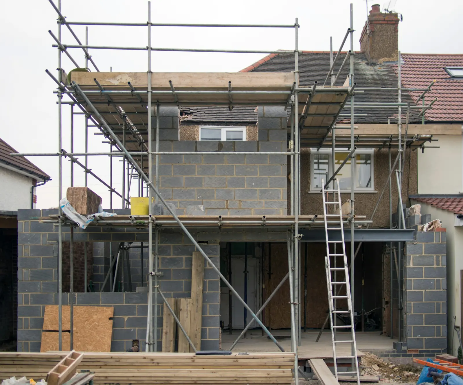 Scaffolding wraps a two-storey blockwork extension, a steel beam carrying the opening across the ground floor.